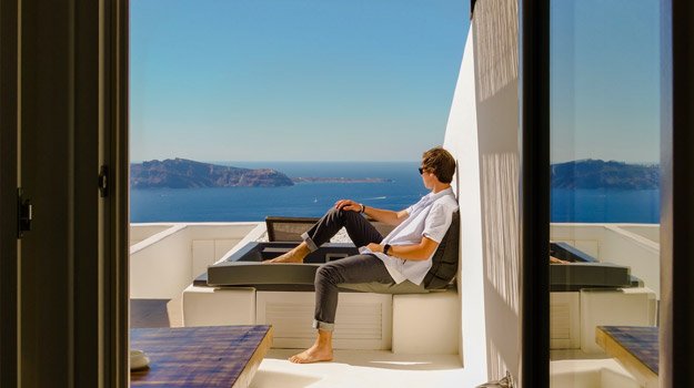 man in white shirt sits outside of a luxury house in front of the sea