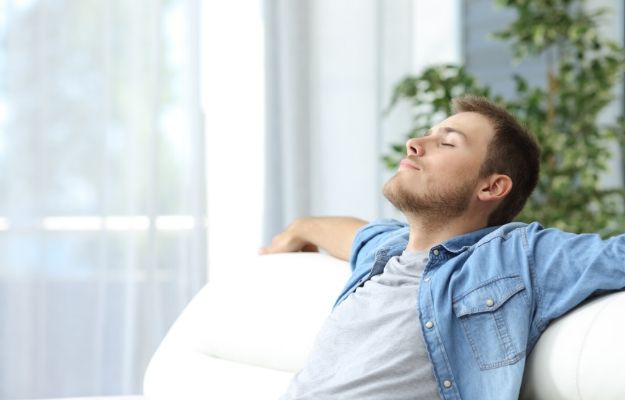 Portrait of a casual tired man resting sitting on a couch at home | Improved Wellness | Get Clarity | How Clarifying The Mind Can Boost Your Health