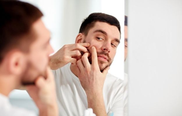 man looking in the mirror and squeezing the acne | Common Causes of Acne in Adult Men | How to Treat Acne in Men Fast