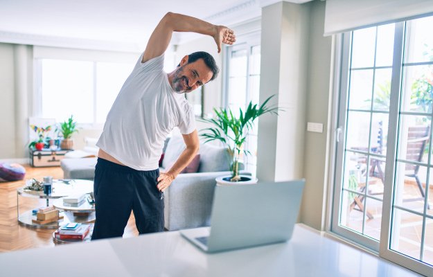 Middle age man with beard training and stretching doing exercise at home looking at sport video on computer | Men’s Path to Improved Health | Benefits of Preventive Health Care