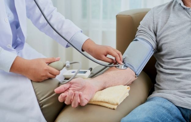 a doctor measuring blood pressure of senior man sitting in couch | Do Not Shy Away From a Doctor | 5 Top Male Health Concerns and What You Can Do