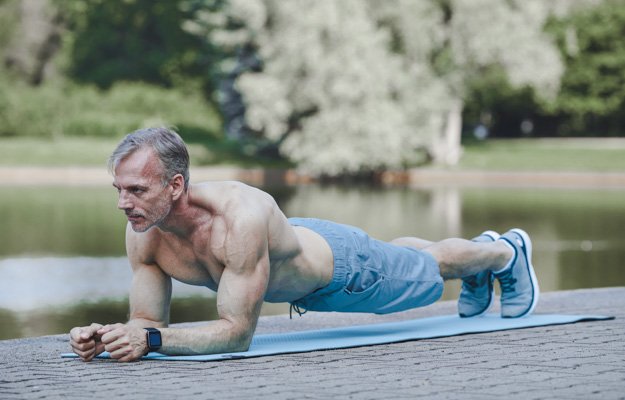 Concentrated muscle bound mature man with shirt doing plank on exercise mat near river | 5 Simple Exercises for Building Muscles