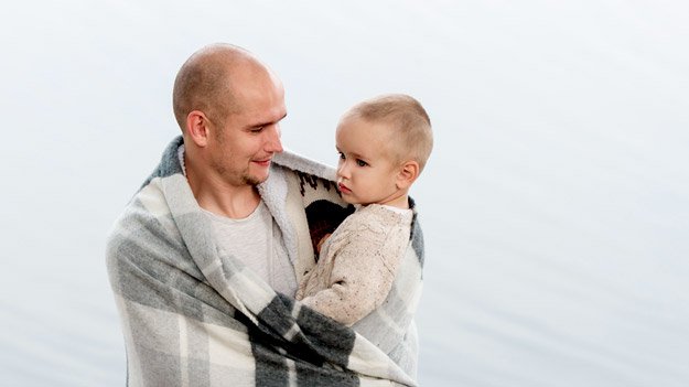 bald-father-holding-infant-son-in-arms-under-big-scarf-ss-alopecia | Male Pattern Baldness Symptoms & FAQ