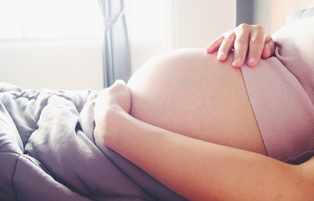 Pregnant woman rest on the bed and hold her hand on her belly | 10 Deadly Disruptors to Your Gut Microbiome