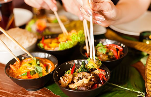 people eating in a Thai restaurant, they eating wi… chopsticks, close-up on hands and food-travel | 10 Deadly Disruptors to Your Gut Microbiome