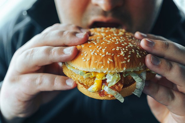 Man-holds-hamburger-in-both-hands-preparing-bite-it-Overfull-ss-body | 3 Ways to Reduce Bloating