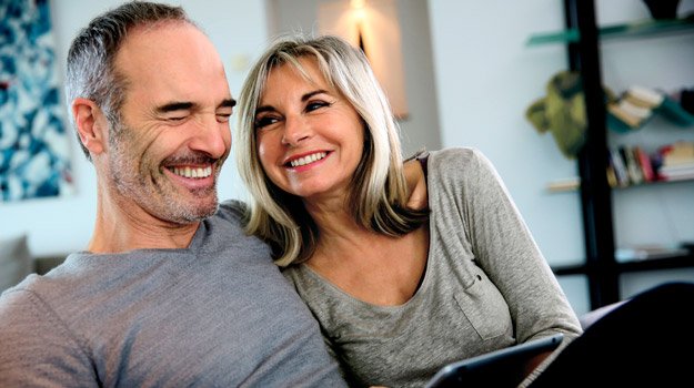Close mature couple laughing together on sofa at home
