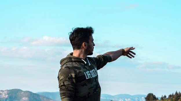 man in army sweatshirt pointing at the sky