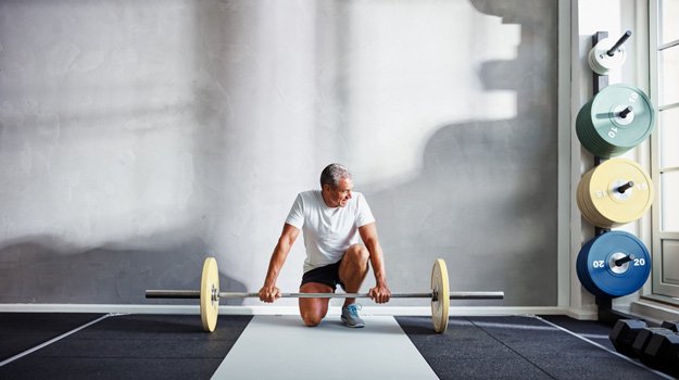 Mature man resting after lifting heavy bar bells